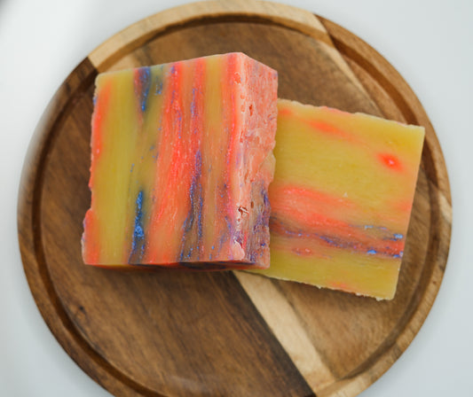 A colorful bar of handmade soap on a wooden cutting board, with swirled patterns of red, orange, yellow, and blue.